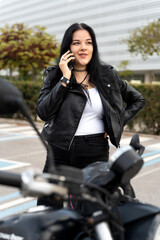 Fototapeta premium Biker woman talking on phone next to motorcycle