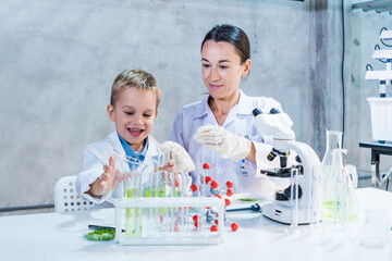 Smiling boy and female mother scientist conducting a fun experiment with test tubes and a microscope in a bright laboratory, showcasing hands-on science learning, mentorship, and curiosity.