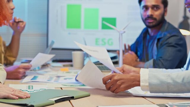 During an office night meeting, multi-ethnic business people intensely brainstorm and focus on paperwork to define goal strategy for a pivotal ESG business shift and agile transformation, driving 