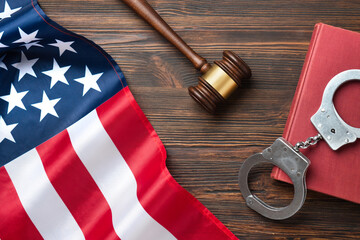Judge gavel, law book and handcuffs with American flag on a wooden desk.