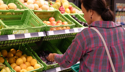 Cheerful 40-year-old woman in casual clothes shops for daily groceries, food items, and other items along the aisles and shelves of grocery store. Healthy eating.