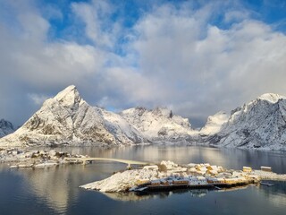 Village of Reine in Lofoten, Norway. Overview of the village, Olstinden mountains and fjord - Reinefjord. Seafront fisherman cabins surrounding the sea.