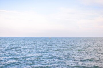Obraz premium The vast expanse of the ocean stretches endlessly beneath a pale blue sky, merging seamlessly at the horizon. 