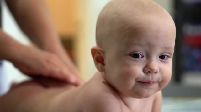 A baby is lying on its back with its head turned to the side. The baby is looking at the camera with a curious expression