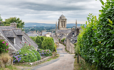 Picturesque street of Locronan with granit houses and hydrangea garden leading to the Saint Ronan Cathedral, int the Finistere department of Brittany, France.