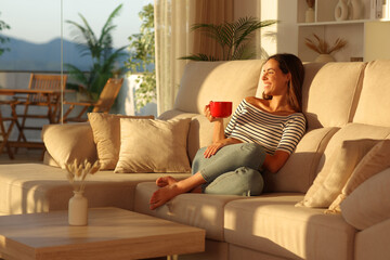 Fototapeta na wymiar Happy woman drinking coffee from red cup in a house