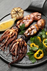 Tasty cooked squids served with lemon, garlic and salad on black table, closeup