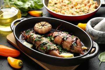Tasty cooked squids with sauce, garlic and products on black table, closeup