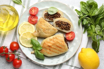 Pieces of tasty grilled squid stuffed with mushrooms, basil, tomatoes and lemon on light grey textured table, flat lay
