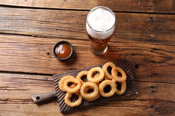 Fried squid rings with sauce and beer served on wooden table, flat lay