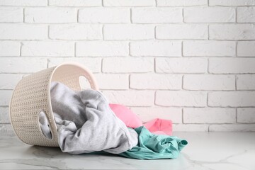 Overturned laundry basket with clothes on white marble surface. Space for text