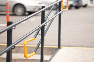 Accessibility ramp with yellow safety handrails near parking area, showing urban inclusive design and accessibility infrastructure.