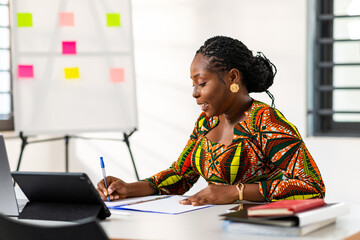 Focused African woman in a modern office, brainstorming ideas with a pen and notebook, embodying...