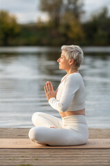 An adult woman in a white suit does yoga by the river