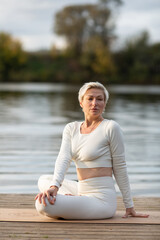 An adult woman in a white suit does yoga by the river
