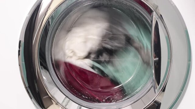 Laundry spinning and washing inside a washing machine, close-up of clothes in motion during wash cycle.