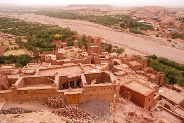 Aerial view of the clay-red fortified village of Aït Benhaddou in Morocco, the terracotta-hued city beside it and distant mountain range beyond – a stunning cultural desert panorama.