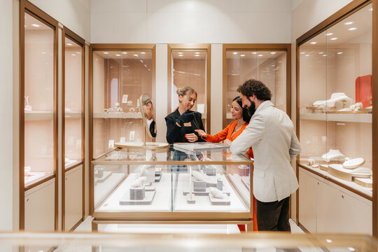 Attractive couple standing at a display counter in an elegant jewelry store, receiving professional assistance from a saleswoman presenting a necklace for purchase