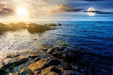 Obraz premium weekend on a rocky beach at the sea. day and night time change concept. beautiful coastline on summer solstice. seascape scenery with clouds above horizon with sun and moon at twilight. mysterious wea