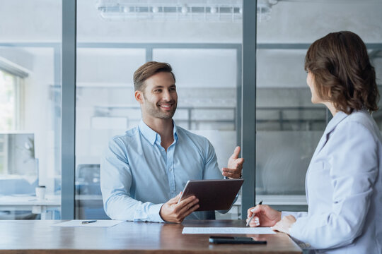 Young real estate manager worker man talking with bank client in office. Business meeting entrepreneur people sitting at table, using gadget tablet device, discussing trade strategy or cv on interview