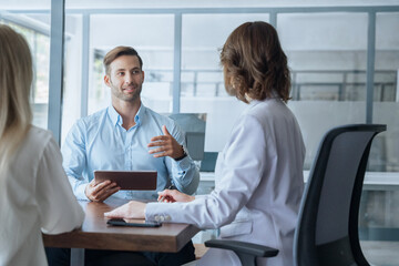 Business meeting of busy entrepreneur people sitting at table, using gadget tablet device, discussing financial trade strategy. Young real estate manager worker man talking with bank client in office