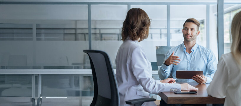 Business meeting of busy entrepreneur people sitting at table, using tablet gadget, discussing financial trade strategy. Young manager worker man talking with bank client in office. Banner, copy space