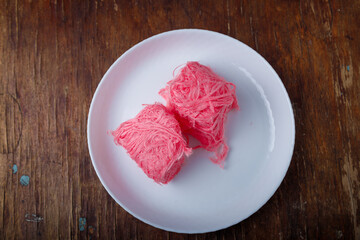 Pismaniye, cotton candy or dragons beard with berries taste on white plate, wooden background. Turkish dessert, light halva, candy floss. Top view, copy space