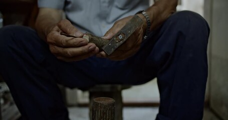 Watch as an experienced craftsman demonstrates his precise skill, hammering a nail into a wooden object with care and focus, highlighting traditional craft and manual labor.