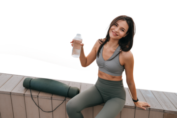 Smiling woman taking a hydration break during a workout, sitting seaside on a wooden deck against transparent background