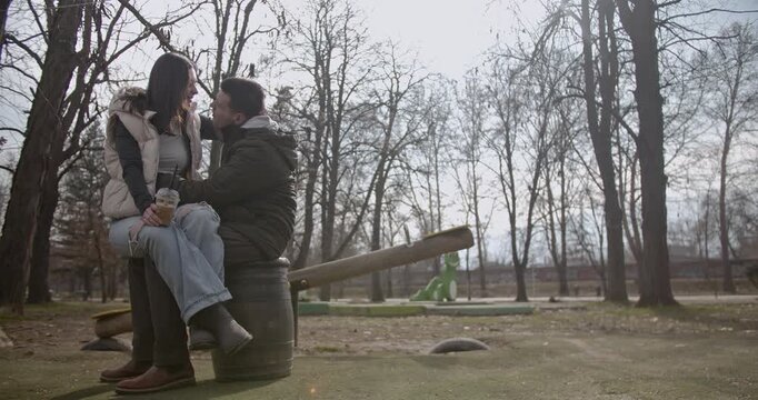 A couple shares an intimate and tender moment, embracing and kissing affectionately in a serene park setting. They are seated closely, showcasing a deep emotional connection and happiness outdoors.