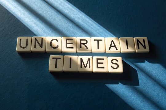 Scrabble Tiles Spell Uncertain Times on Blue Surface with Dramatic Light