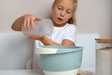 Child baking. Girl pours water into bowl.