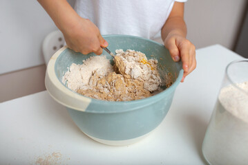 Child mixes dough in a bowl. Home baking for family.