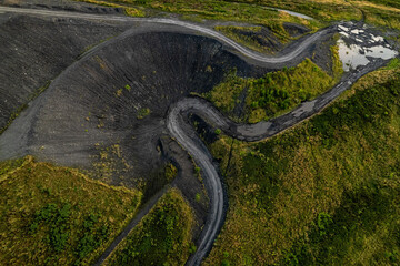Naklejka premium Winding asphalt road through coal mining waste dump aerial view Rybnik Poland horizontal black slag heap green vegetation industrial landscape