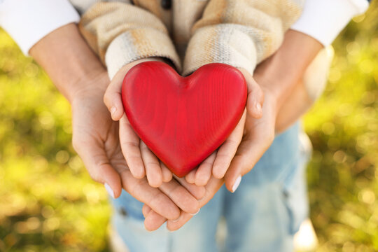 Mother with her son holding red wooden heart together outdoors, closeup. Family bonding