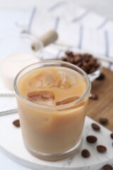 Tasty iced coffee with milk and beans on white table, closeup
