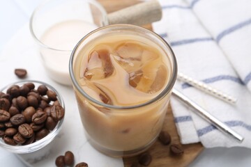 Tasty iced coffee with milk and beans on white table, closeup