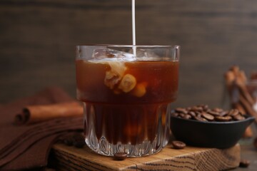 Pouring milk into iced coffee at wooden table, closeup