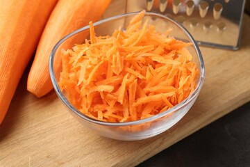 Whole and grated carrots and grater on grey table, closeup