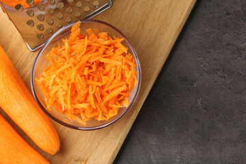 Whole and grated carrots and grater on grey table, flat lay. Space for text