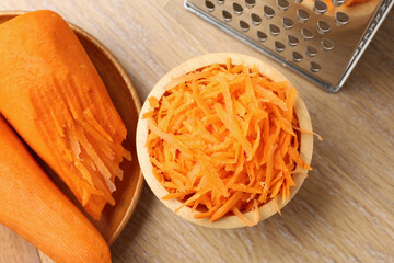 Whole and grated carrots and grater on wooden table, flat lay