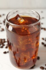 Tasty iced coffee and beans on white wooden table, closeup