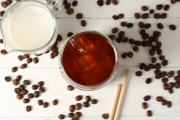 Tasty iced coffee, milk and beans on white wooden table, flat lay