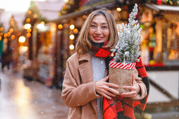 Woman smiling with a holiday plant at a festive market during winter season