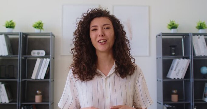 Video call and online speech of confident businesswoman from office workplace. Happy woman speaker waving hand to say Hi with smile, involved person talking to colleagues in webinar, video chat
