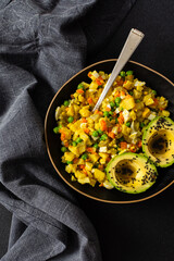 A colorful salad combines boiled egg, tender chicken breast, diced potatoes, vibrant carrots, and fresh green peas, topped with creamy avocado and sesame seeds, all drizzled with olive oil