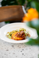 A plate with a large potato pancake topped with a rich meat stew and garnished with fresh herbs, served alongside sliced pickles on a speckled stone countertop.