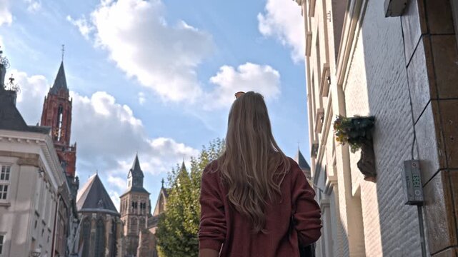 Woman in Vrijthof square on a sunny day, the historic center of Maastricht, Netherlands. The background is dominated by the iconic red tower of the Sint-Janskerk (St. John's Church).