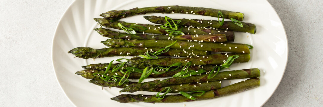 Steamed asparagus spears topped with fresh herbs are arranged neatly on a white plate. The dish appears vibrant and is suitable for a healthy meal or side, banner - Powered by Adobe