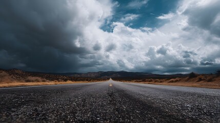 An empty asphalt highway stretches through a desolate desert landscape leading towards a vast horizon under a dramatic sky with ominous storm clouds